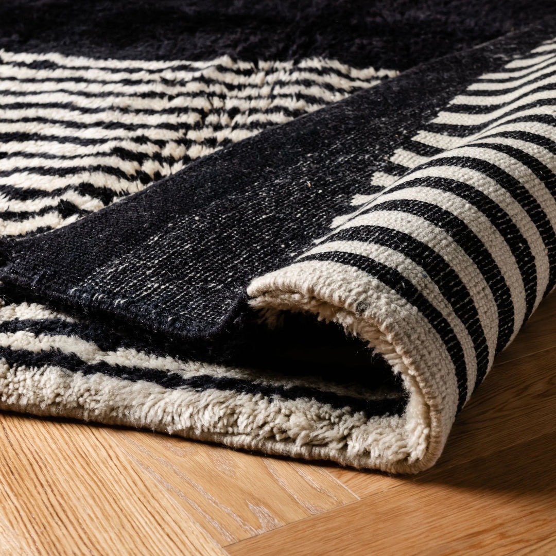 Black and white geometric Moroccan wool rug on wooden floor, showcases modern abstract design and traditional craftsmanship.
