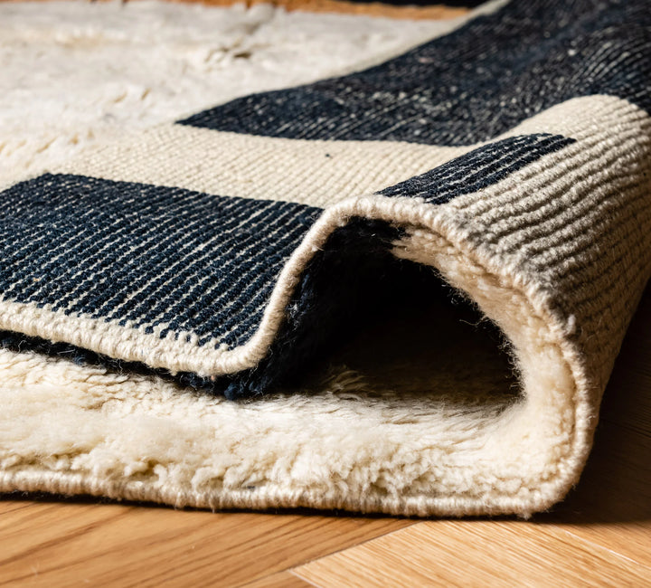 Close-up of a modern geometric Moroccan wool rug with black, ivory, and amber blocks, showcasing plush texture and craftsmanship.