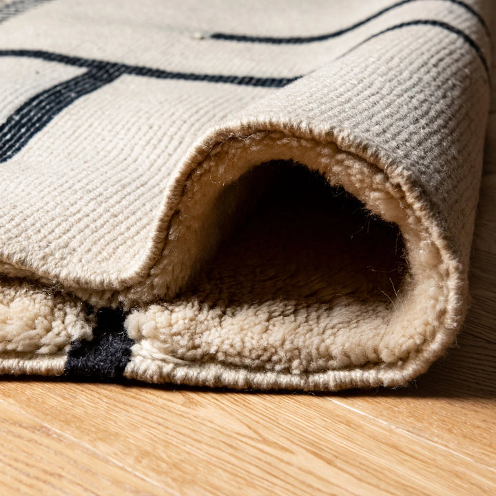 Close-up of a modern black and white wool Moroccan rug with a lined pattern, showcasing texture and craftsmanship.