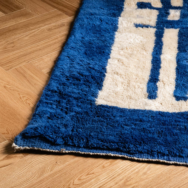 Blue Moroccan wool rug with geometric Berber design on wooden floor, perfect for a modern boho or contemporary home decor.