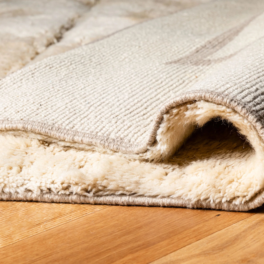Close-up of Neutral Beni Mrirt Moroccan wool rug with triangle motif, showcasing its rich texture and craftsmanship on hardwood floor.