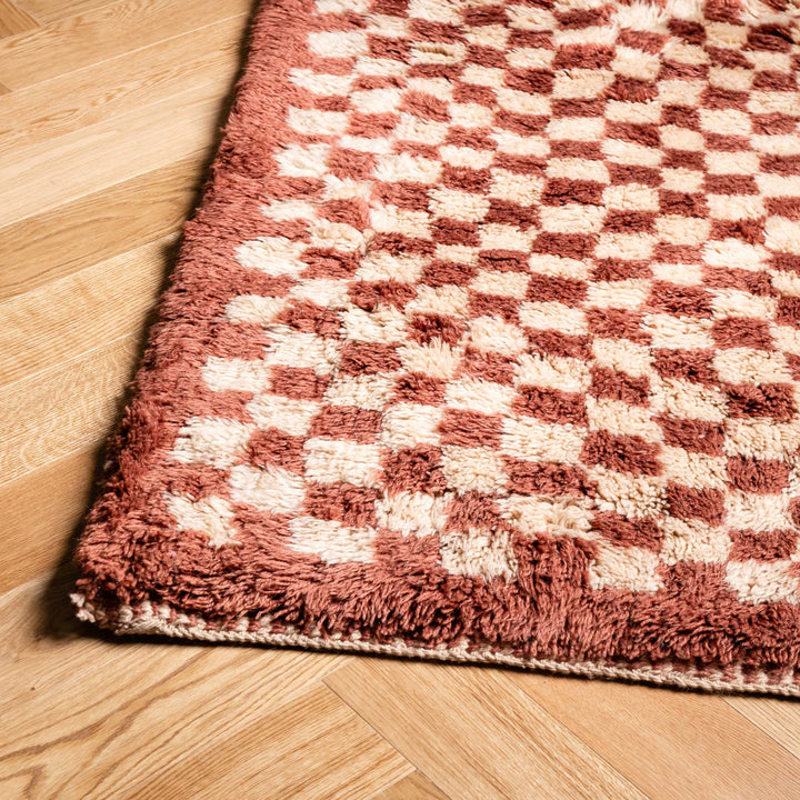 Red checkerboard Moroccan shag wool rug on wood floor, handmade in Berber style, perfect for cozy living rooms and boho decor.