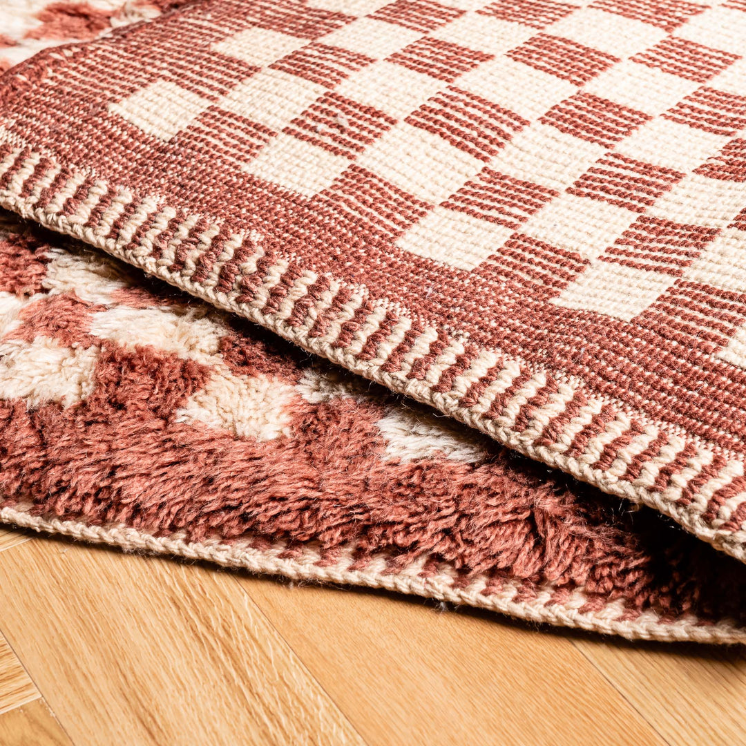 Close-up of red checkerboard Moroccan wool rug with plush shag texture, showcasing traditional handmade craftsmanship.