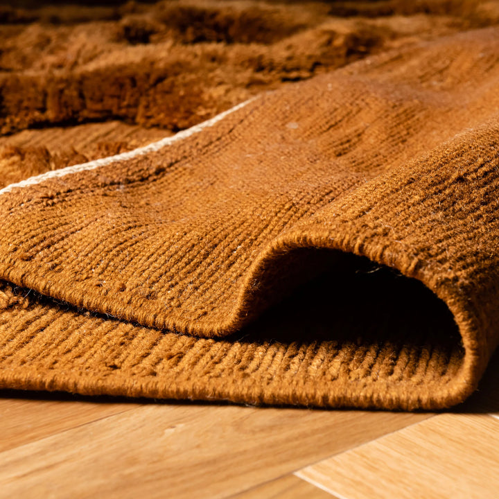 Close-up of a rust brown Moroccan Beni Mrirt wool rug with a diamond design on a wooden floor, showcasing plush texture and intricate patterns.