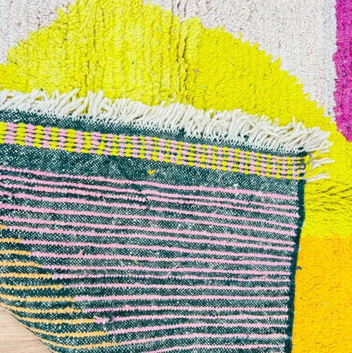 Close-up of a vintage abstract Moroccan wool rug in vibrant pink, yellow, and cream with geometric patterns and fringe.