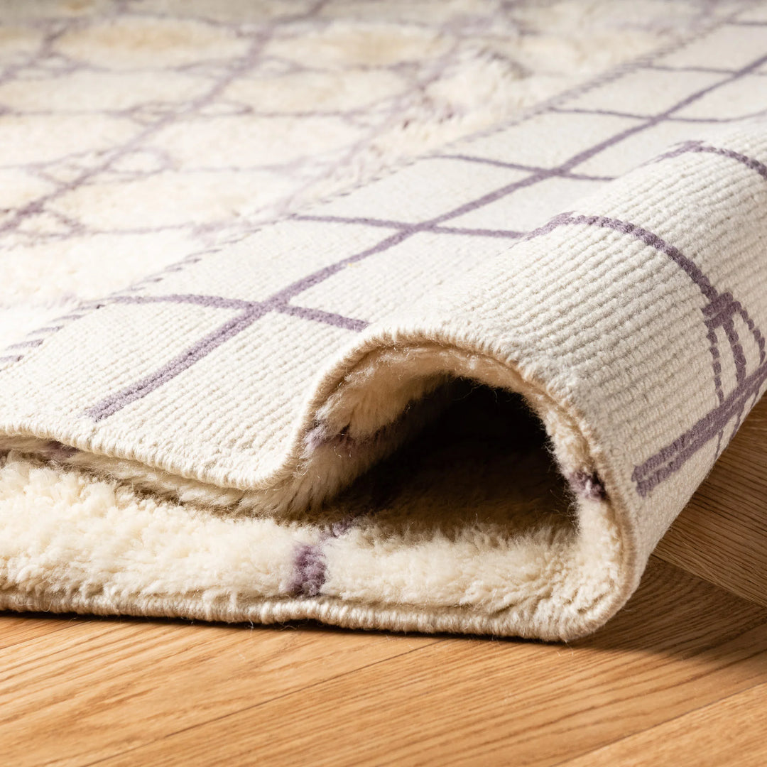 Soft Beni Ourain Moroccan rug with lavender diamond circles on a natural wool texture, rolled on wooden floor.
