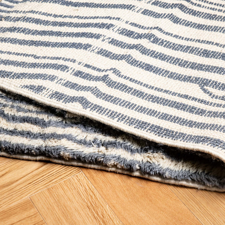 Striped Moroccan wool rug with taupe and blue gradient tones on a cream base, showcasing ripple texture.