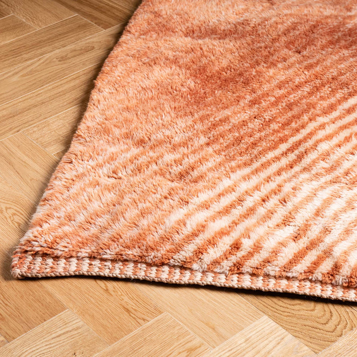 Terracotta Chevron Moroccan Wool Rug on wooden floor, highlighting rich earthy colors and plush texture. Handmade Moroccan decor piece.