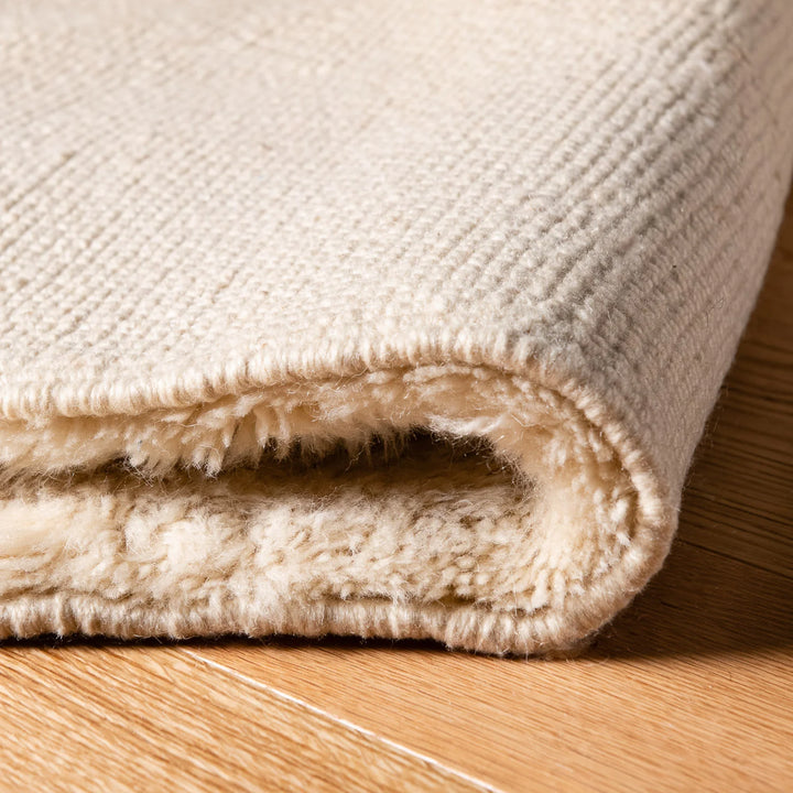 Close-up of folded tone-on-tone Moroccan wool rug with minimalist mountain design on hardwood floor.