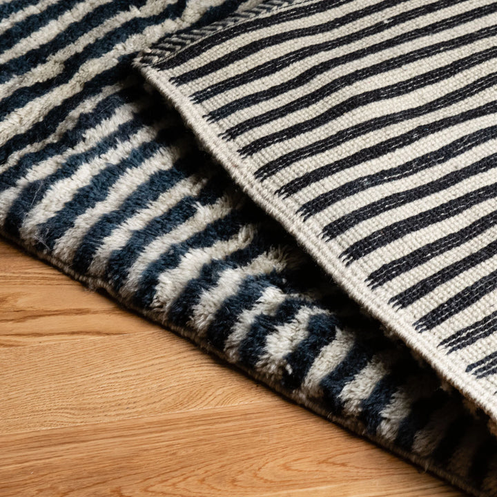 Wavy Striped Moroccan Wool Rug with black and ivory pattern on wooden floor, handmade for bohemian and minimalist decor.