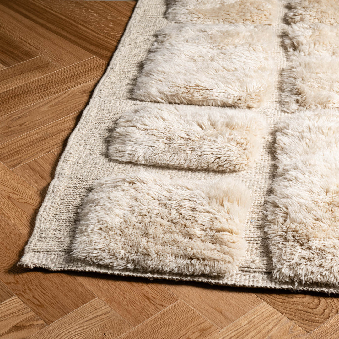 White Moroccan wool rug with check grid pattern, handmade by Berber artisans, on wooden floor; perfect Moroccan shag and area rug.