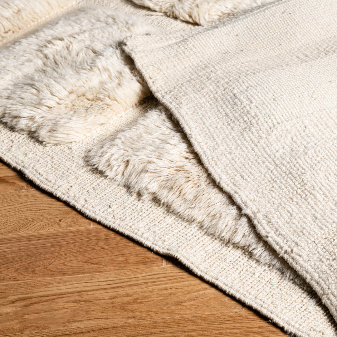 Close-up of a white Moroccan wool rug with a plush texture, handmade Berber carpet on a wooden floor, ideal for modern interiors.