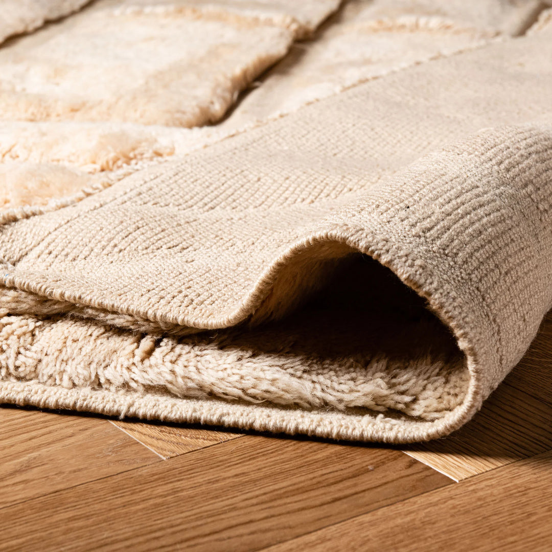 Folded edge of a white Moroccan wool rug with textured design, ideal for modern and bohemian interiors. Handmade Berber shag carpet.