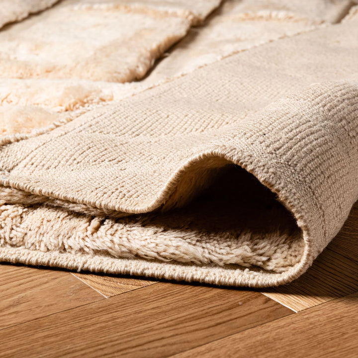 Folded edge of a white Moroccan wool rug with textured design, ideal for modern and bohemian interiors. Handmade Berber shag carpet.