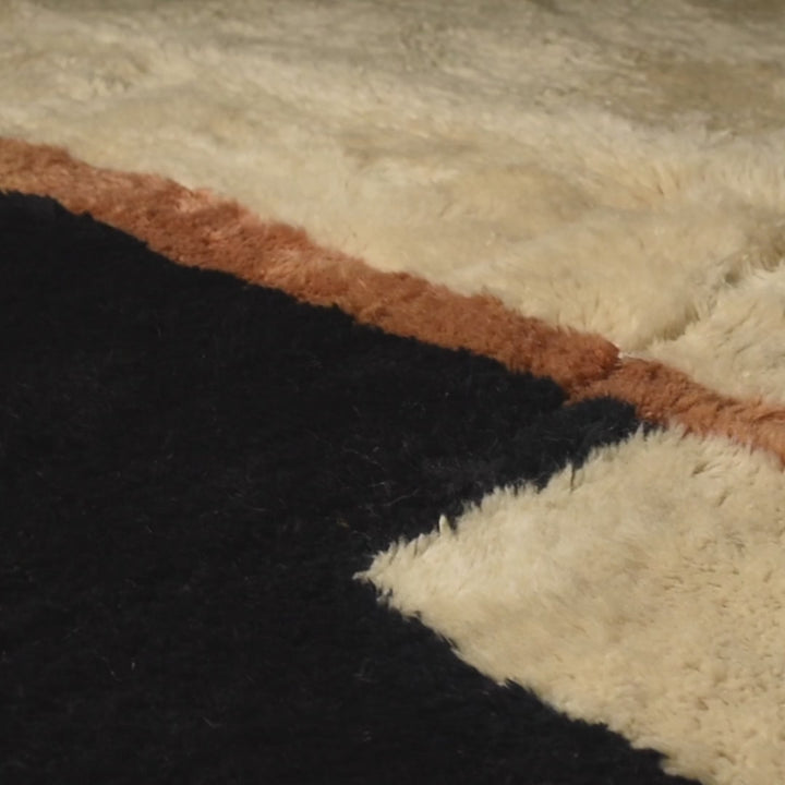 Close-up of modern Moroccan Beni Mrirt rug with black, ivory, and amber geometric blocks; wool texture for contemporary interiors.