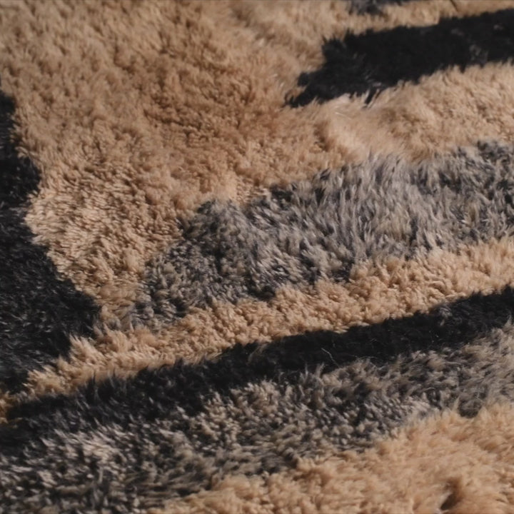 Close-up of a handmade Moroccan wool rug with bold geometric patterns in black and beige, showcasing plush texture.