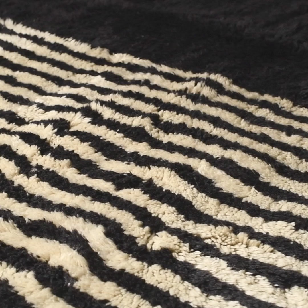 Handwoven Moroccan rug with black and white geometric design, crafted from wool, perfect for modern or traditional interiors.