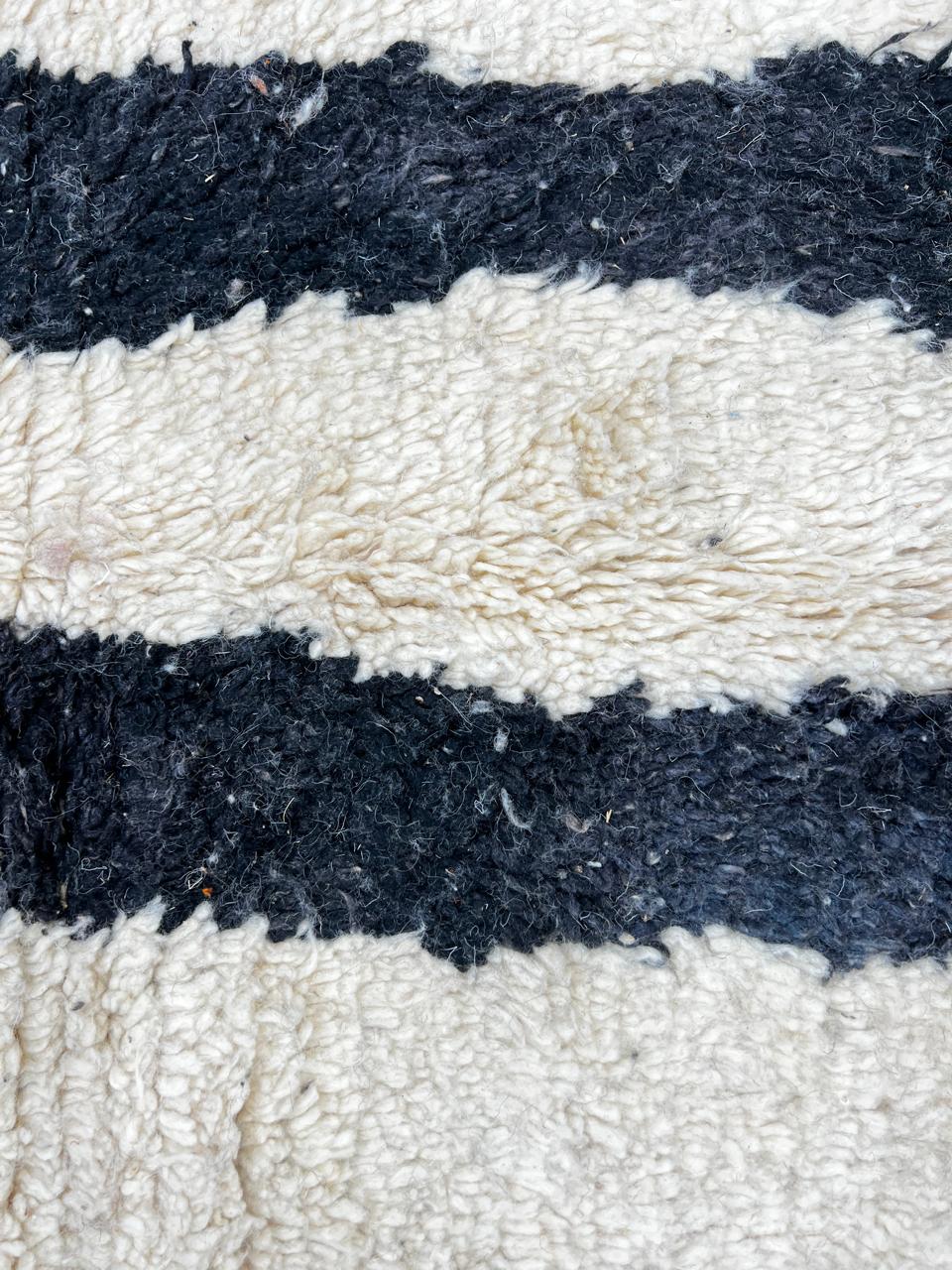 Handmade abstract Moroccan runner rug with black and burnt orange vertical stripes on a white wool base.