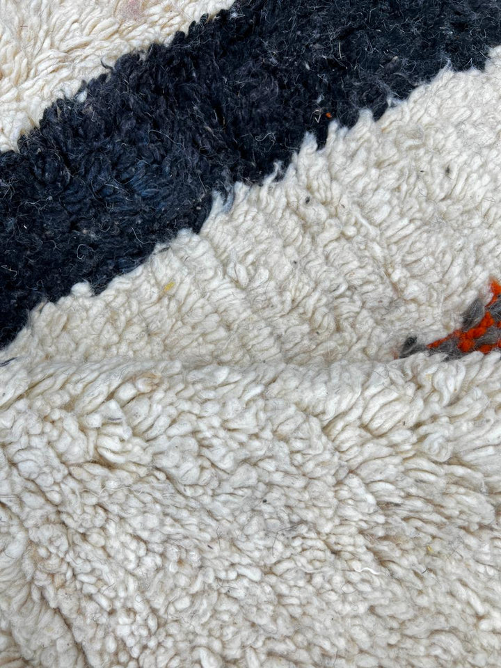 Handmade abstract Moroccan runner rug with black and burnt orange vertical stripes on a white wool base.