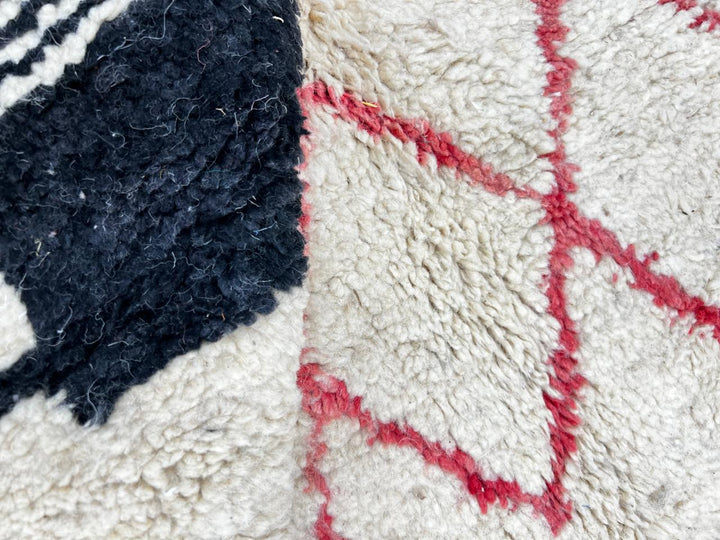 Handmade white Moroccan runner rug with red and black abstract geometric patterns in natural wool.