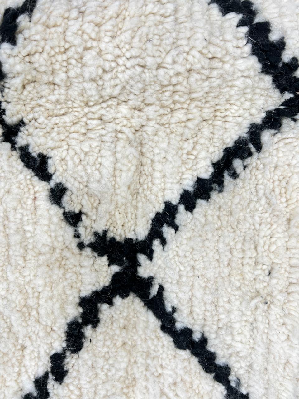 Handmade Beni Ourain Moroccan wool rug with black diamond lines on a natural white wool background.