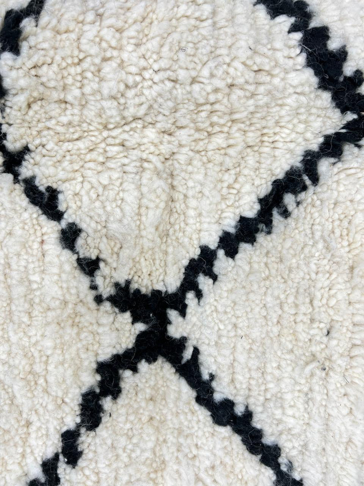 Handmade Beni Ourain Moroccan wool rug with black diamond lines on a natural white wool background.