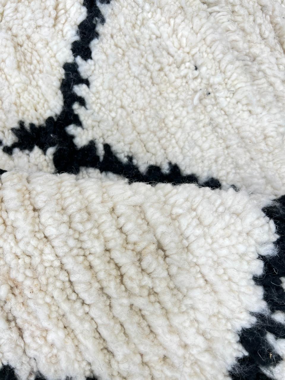 Handmade Beni Ourain Moroccan wool rug with black diamond lines on a natural white wool background.