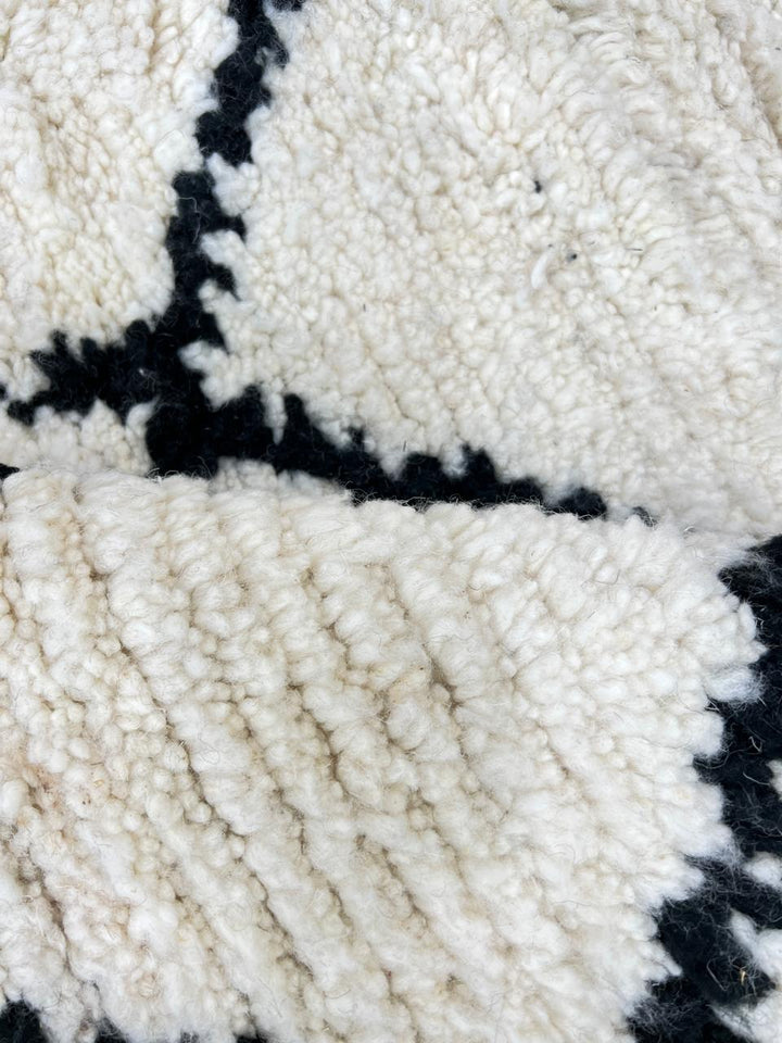 Handmade Beni Ourain Moroccan wool rug with black diamond lines on a natural white wool background.