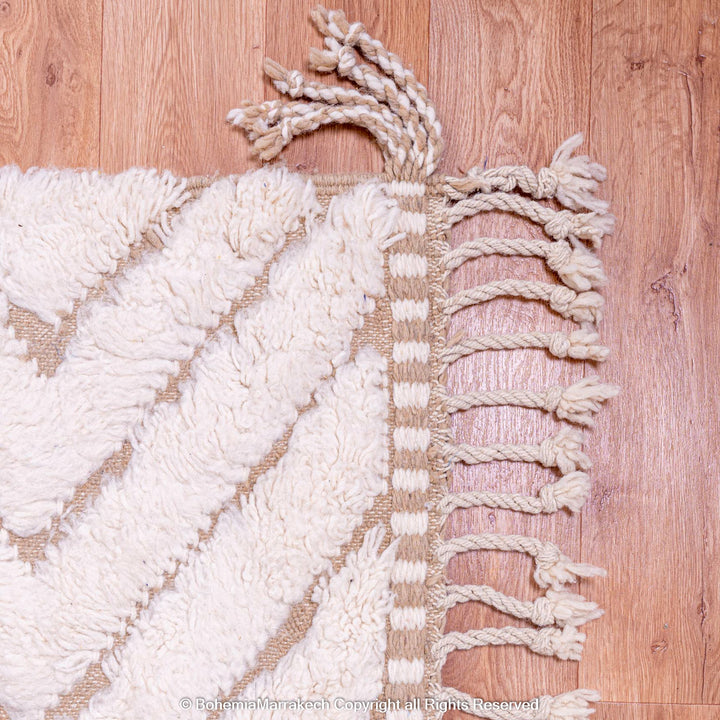 White handmade Beni Ourain Moroccan rug with geometric pattern, showcasing fringed edge on wooden floor.
