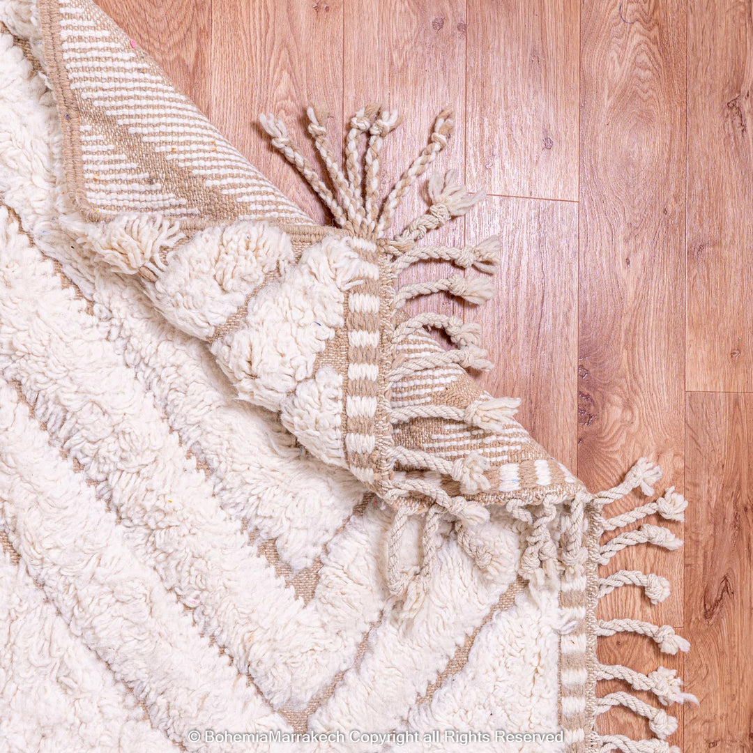 Handmade Beni Ourain Moroccan wool rug with geometric pattern, beige and white tones, displayed on wooden floor.