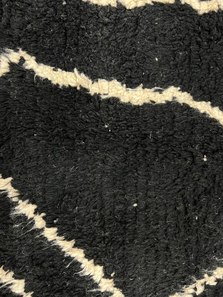 Round black Moroccan wool rug with beige abstract line design.