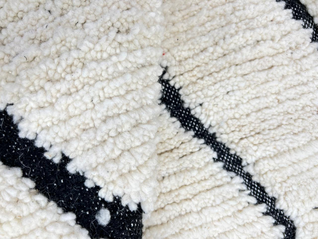 Handmade Moroccan runner rug with black geometric diamond pattern on a white wool background.