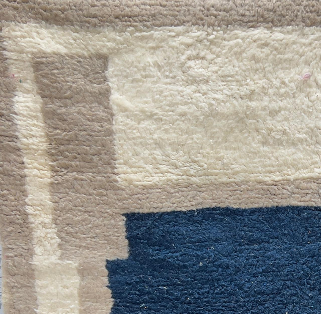 Round Moroccan wool rug with a navy blue center and beige geometric border.