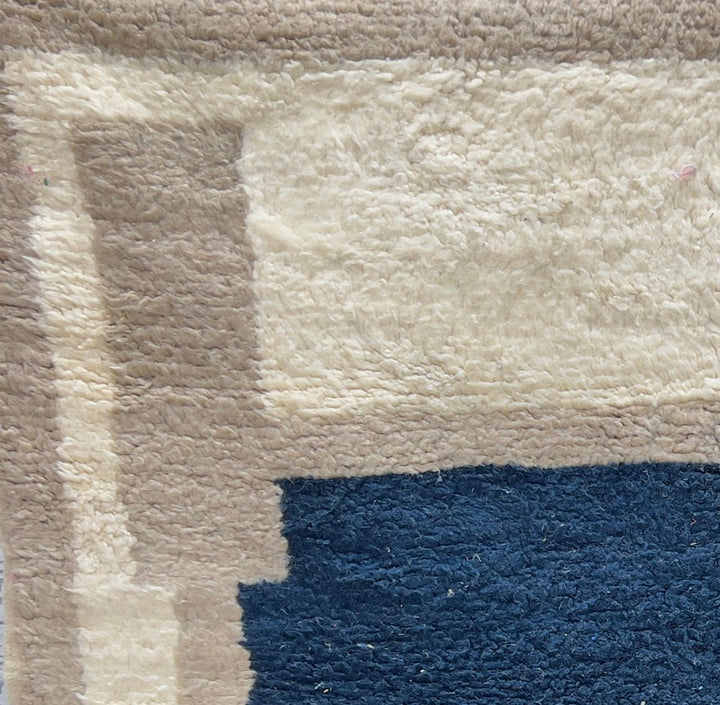 Round Moroccan wool rug with a navy blue center and beige geometric border.