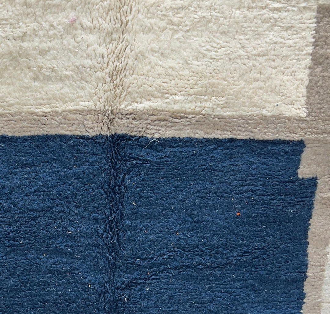 Round Moroccan wool rug with a navy blue center and beige geometric border.