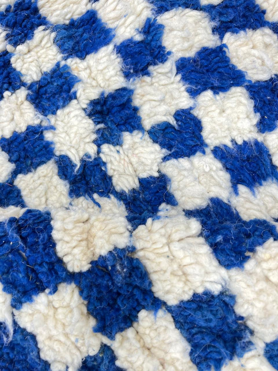 Handmade Moroccan wool rug with blue and white checkerboard pattern, round shape, and soft plush texture.