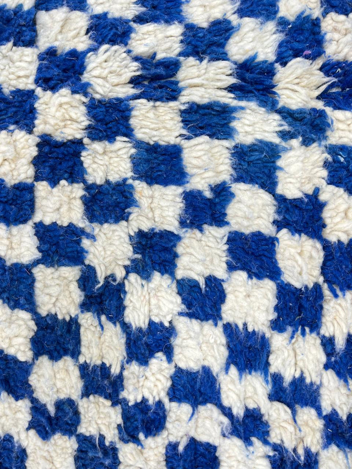Round Moroccan wool rug with blue and white checkerboard pattern on a white background