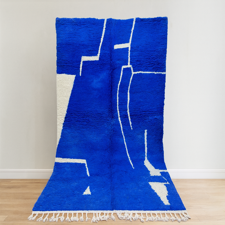 Blue and white geometric-patterned rug on a wooden floor with a white wall background