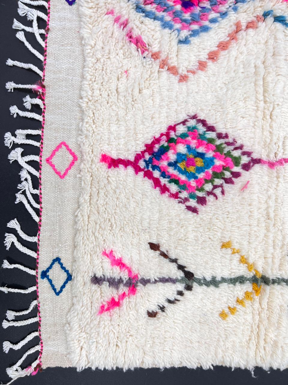 Colorful handmade Moroccan Berber rug with diamond tribal patterns on white wool