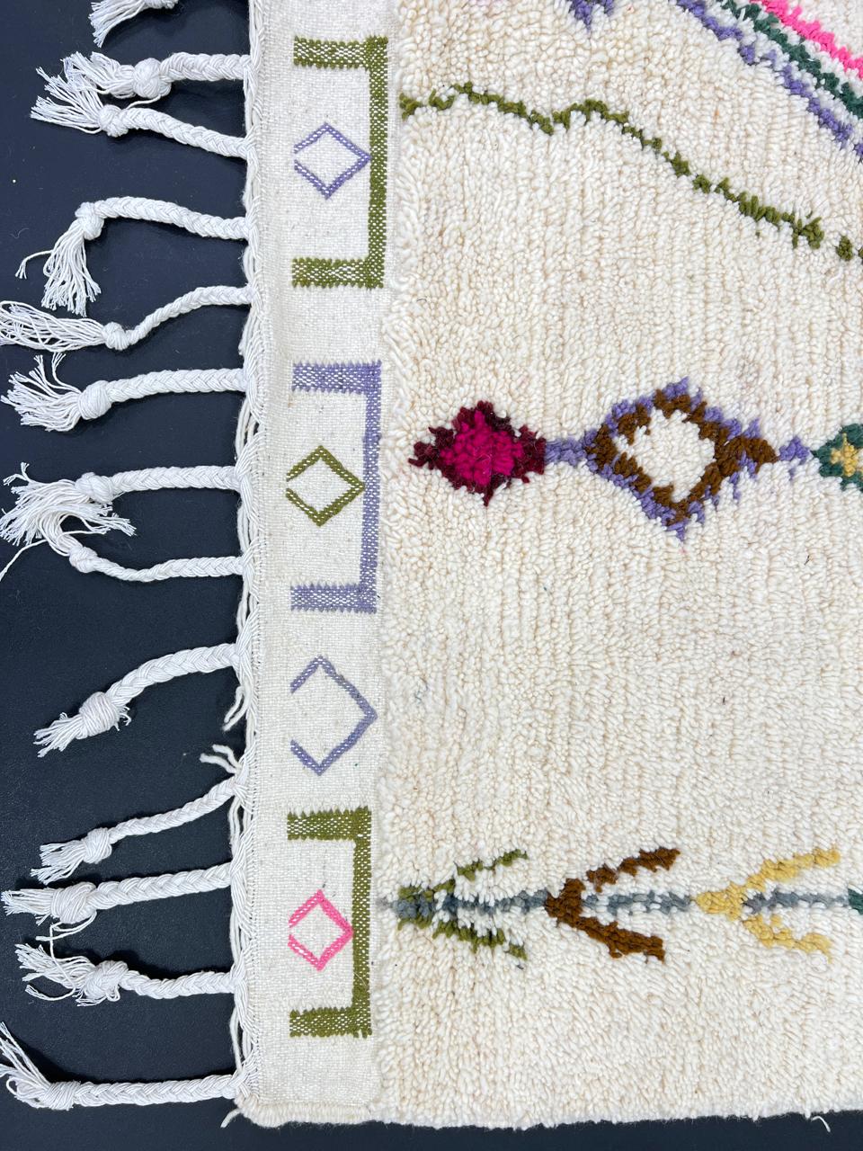 Handmade Moroccan runner rug with colorful geometric and tribal motifs on a white wool background, crafted by Berber artisans.