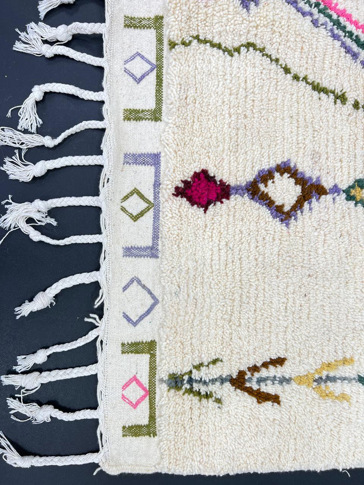 Handmade Moroccan runner rug with colorful geometric and tribal motifs on a white wool background, crafted by Berber artisans.