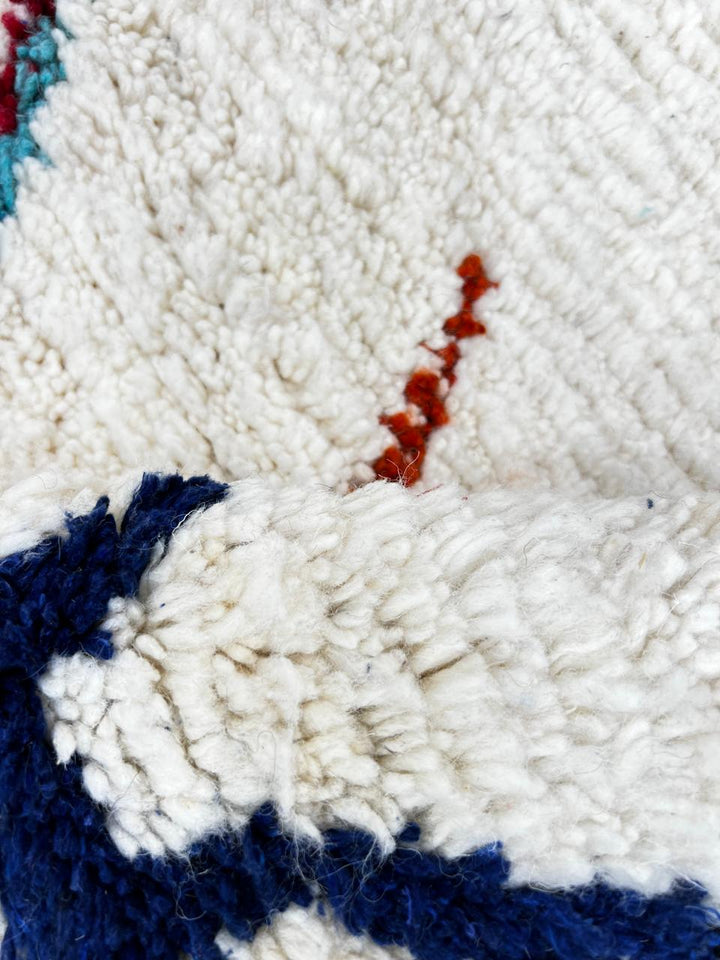 Handmade colorful Moroccan wool runner rug with blue, red, and orange geometric diamond patterns on a white base.