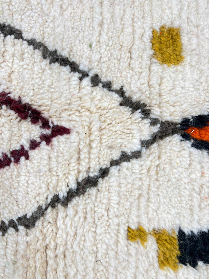 Handmade Moroccan runner rug with colorful geometric symbols, abstract lines, and dotted accents on a white wool background.