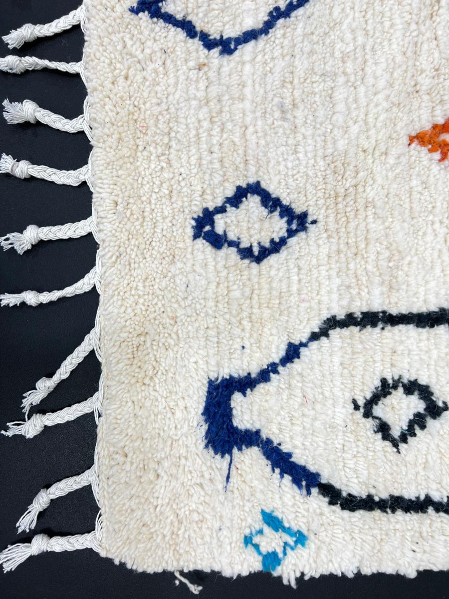 Handmade colorful Moroccan wool runner rug with blue, red, and orange geometric diamond patterns on a white base.