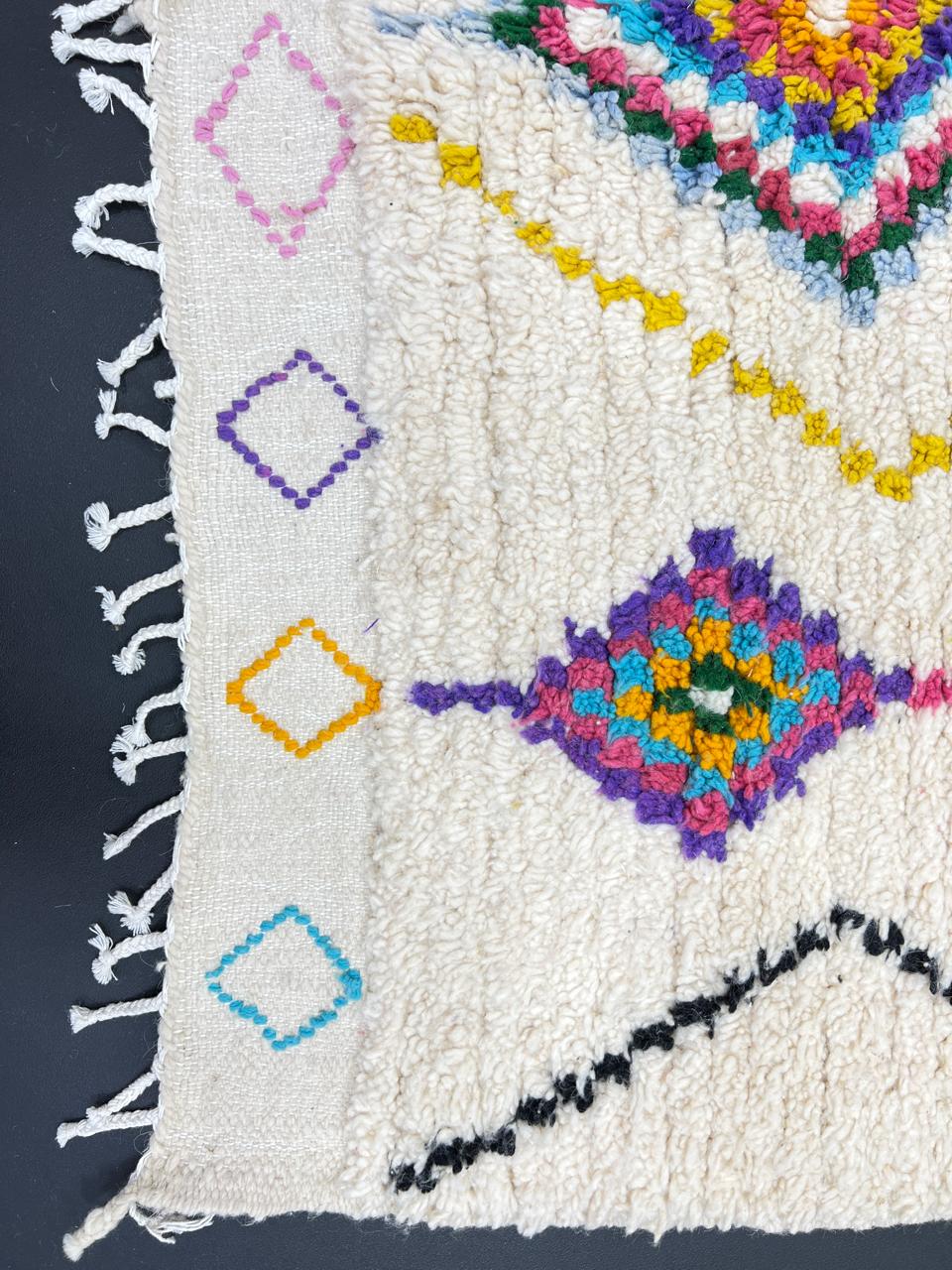 Colorful handmade Moroccan Berber wool rug with vibrant diamond patterns on ivory background