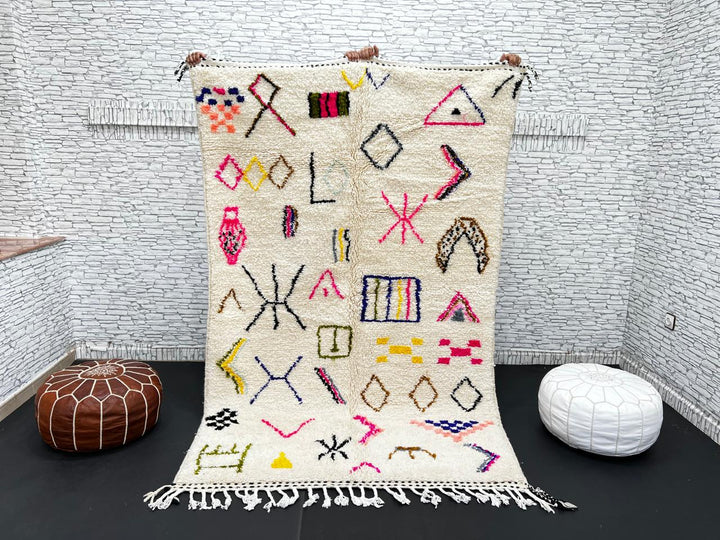 Handwoven Moroccan wool rug with cream background and colorful geometric Berber motifs in pink, blue, green, and yellow