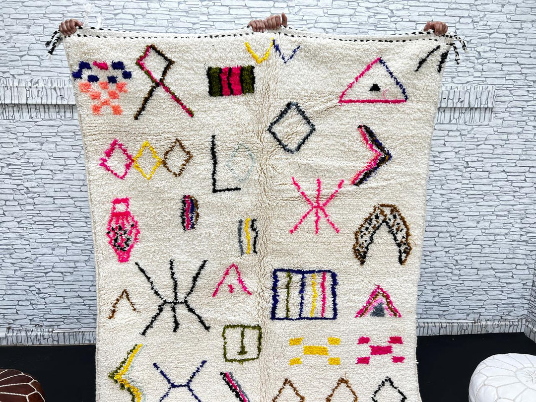 Handwoven Moroccan wool rug with cream background and colorful geometric Berber motifs in pink, blue, green, and yellow