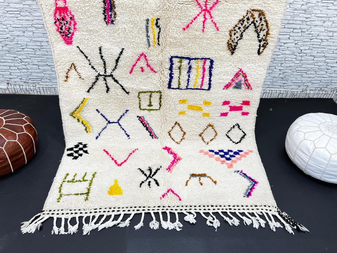 Handwoven Moroccan wool rug with cream background and colorful geometric Berber motifs in pink, blue, green, and yellow