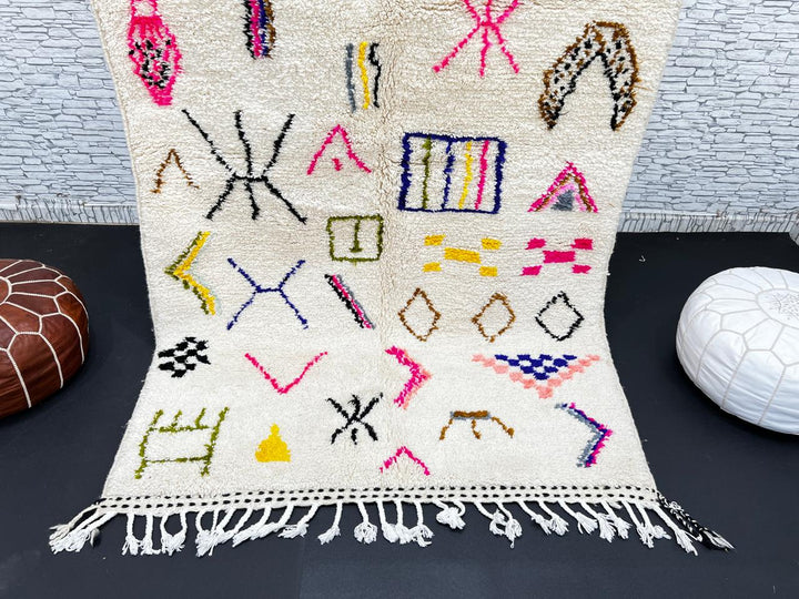 Handwoven Moroccan wool rug with cream background and colorful geometric Berber motifs in pink, blue, green, and yellow