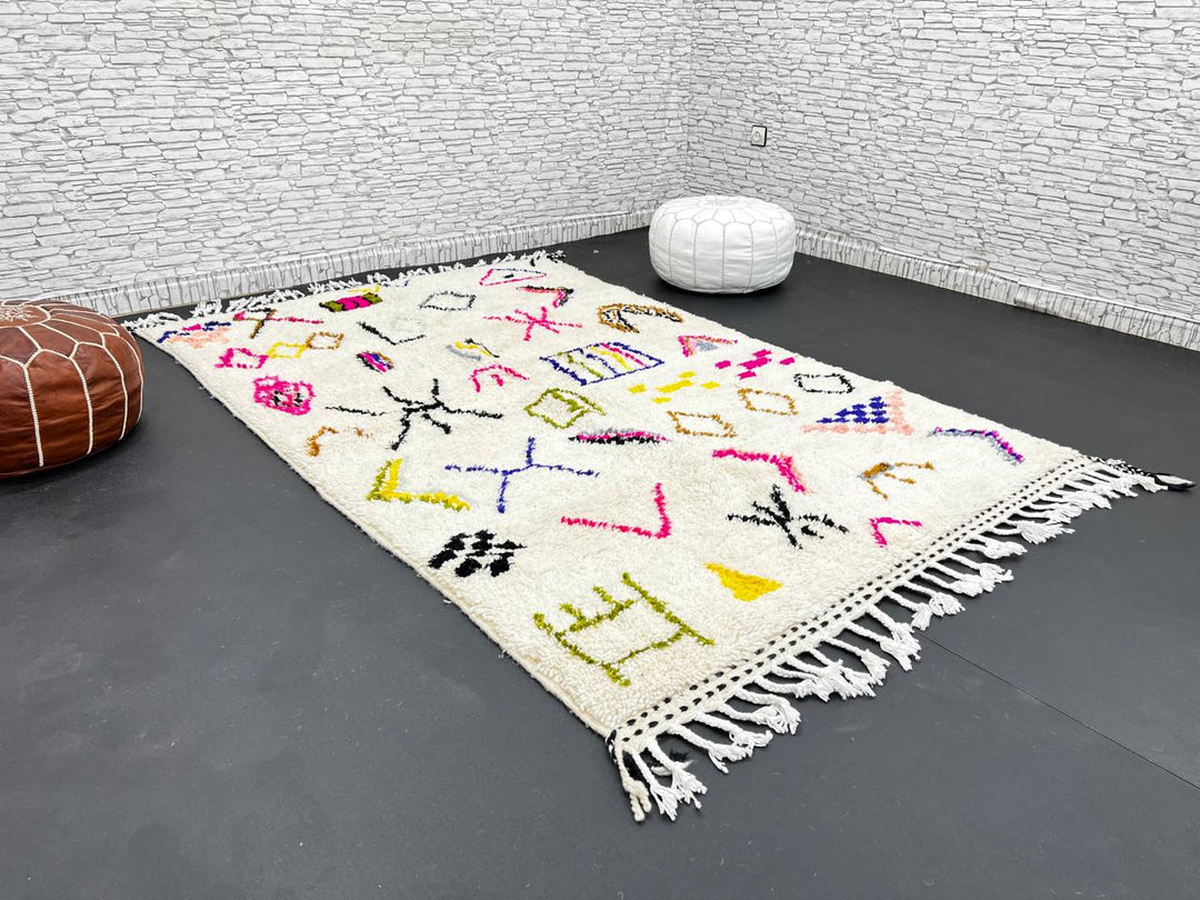Handwoven Moroccan wool rug with cream background and colorful geometric Berber motifs in pink, blue, green, and yellow